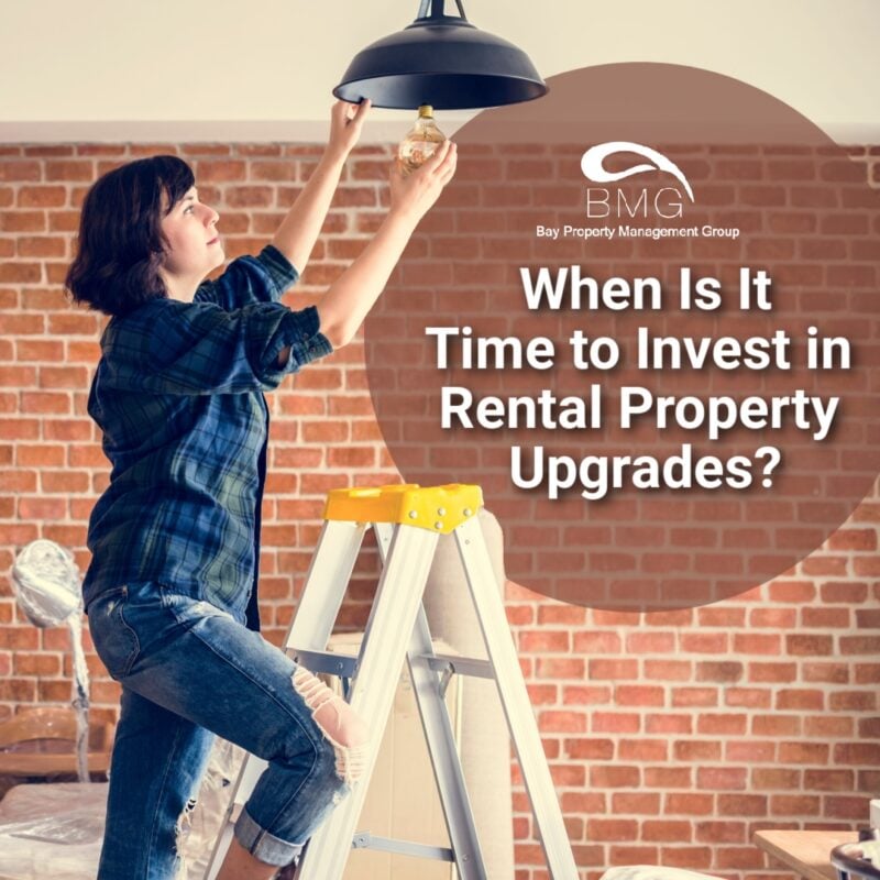 Woman on a ladder changing a lightbulb in front of a brick wall and home remodeling materials.