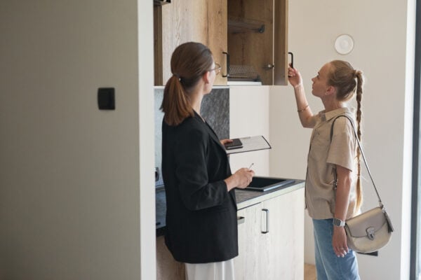 Waist up portrait of female real estate agent giving apartment tour to young woman.