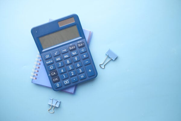 Close up of blue calculator and notepad on color background.