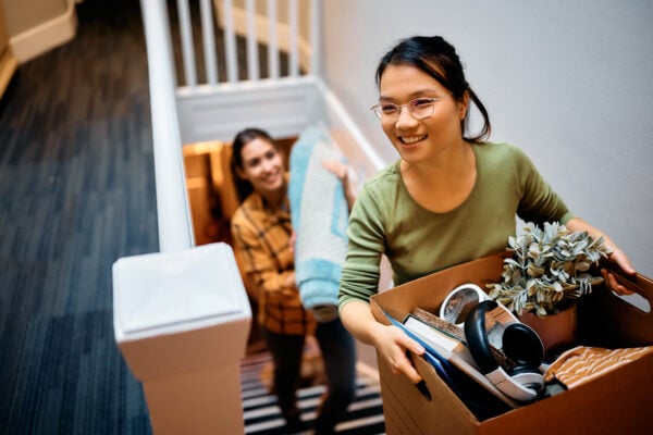 Happy woman and her friend walking upstairs through hallway while moving in new apartment.