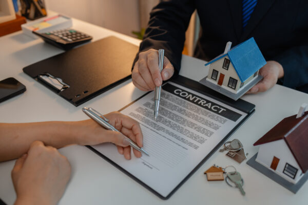 Two people reviewing and signing a real estate contract with a model house on the table, symbolizing legal asset protection.