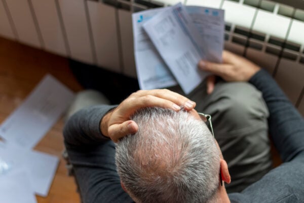 Person sitting indoors looking stressed while holding electricity bills and utility statements.
